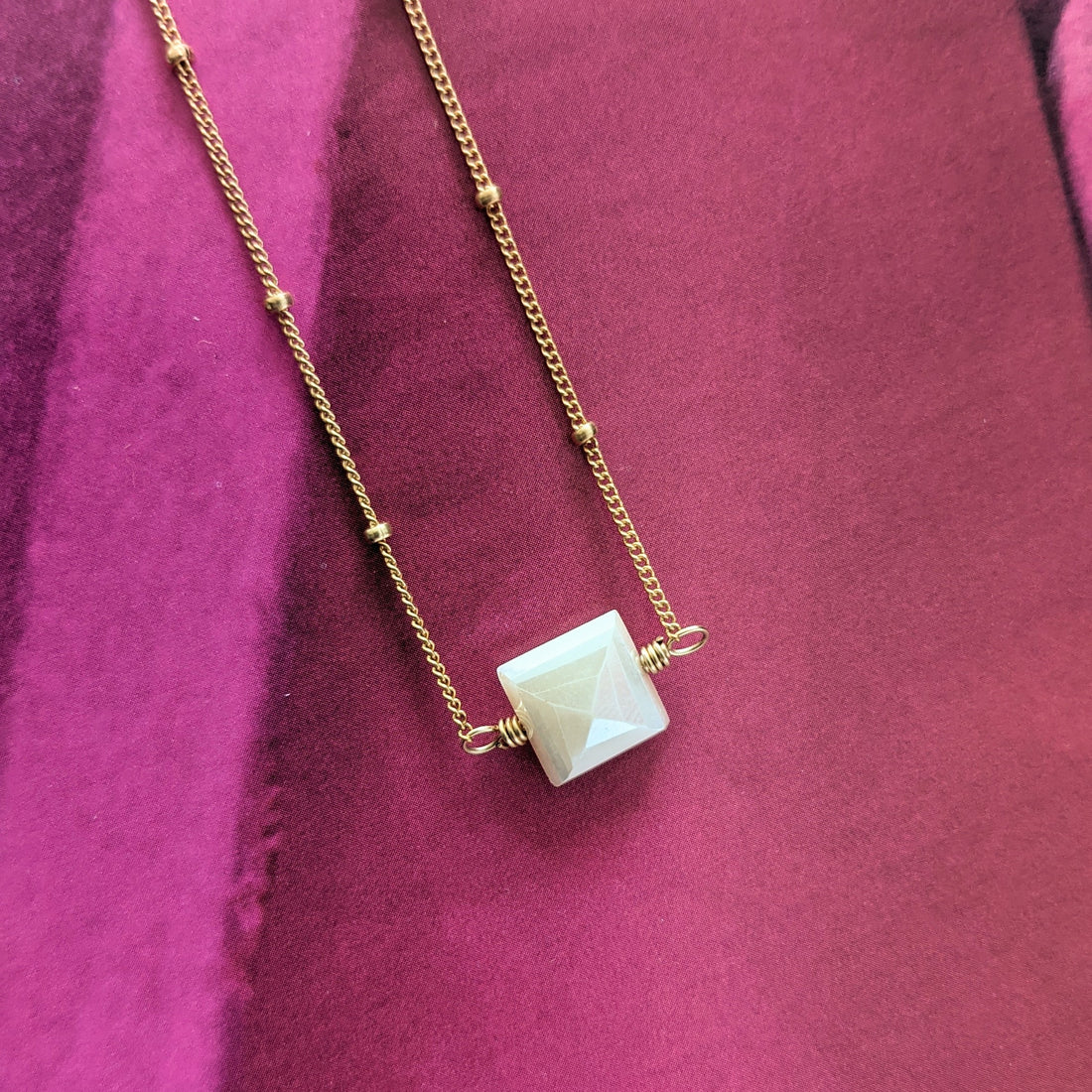 Close up of peach moonstone necklace in 14K gold fill beaded satellite chain angled slightly on bright pink background