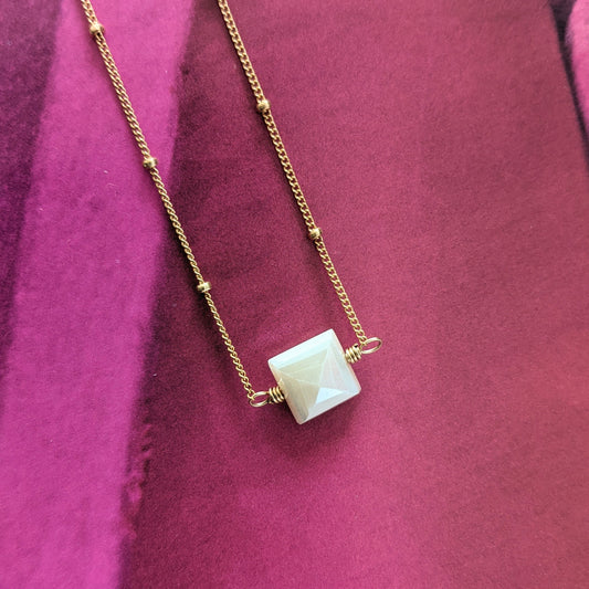 Close up of peach moonstone necklace in 14K gold fill beaded satellite chain angled slightly on bright pink background