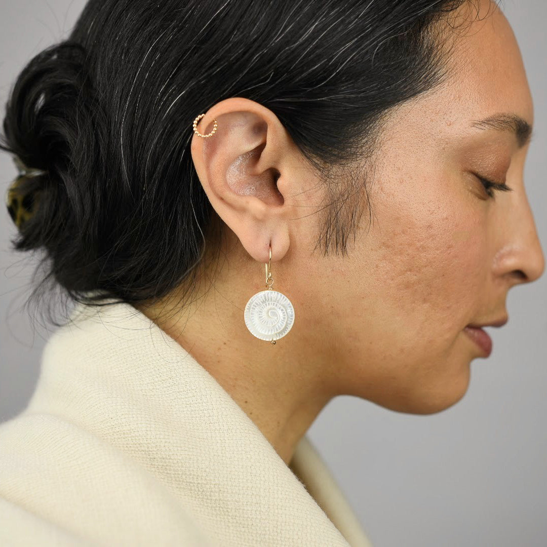Close up image of a model wearing 14K gold filled Mother of Pearl Spiral Earrings from Zurina Ketola