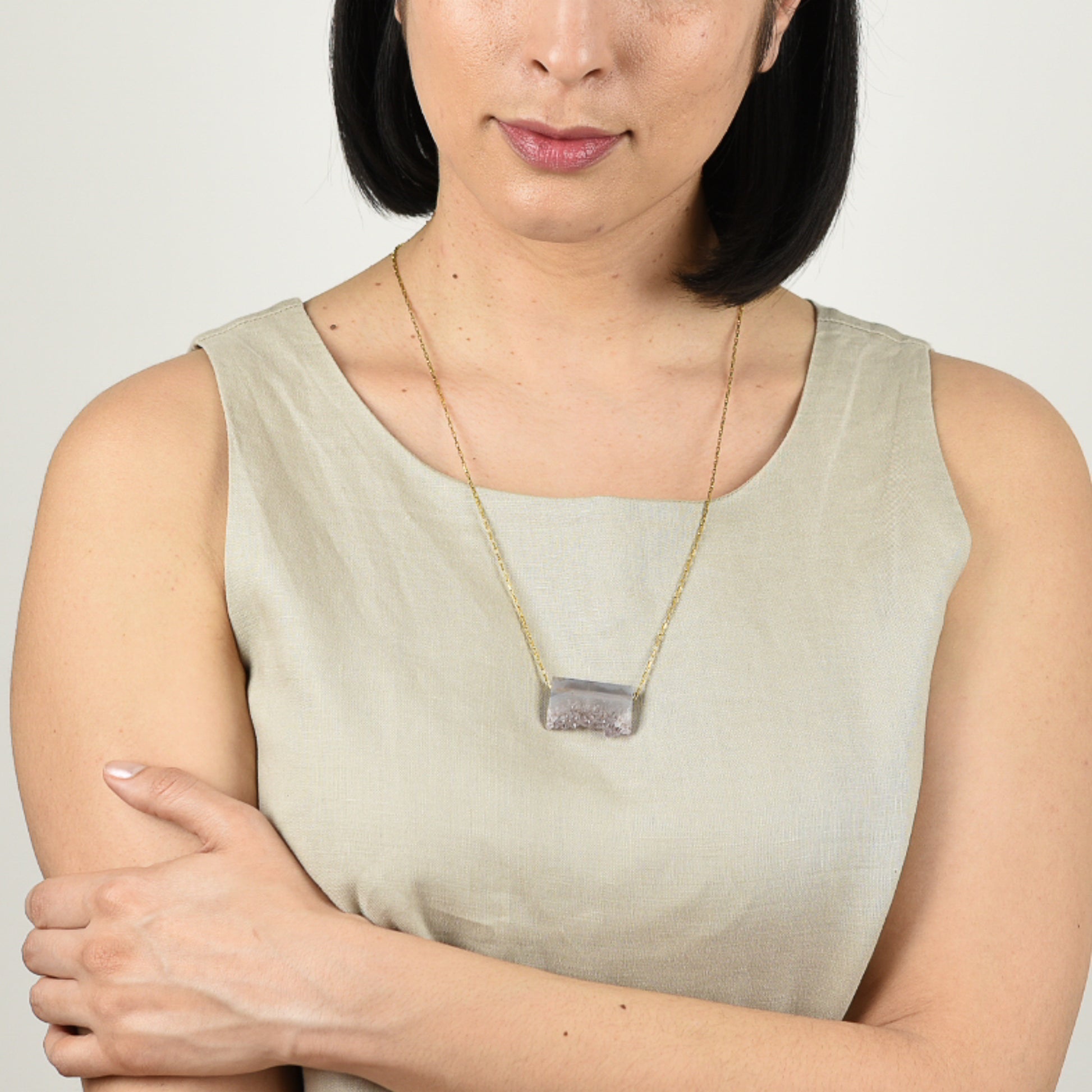 Model with mid tone skin and shoulder length black hair in beige linen tank top wearing long amethyst druzy necklace.  