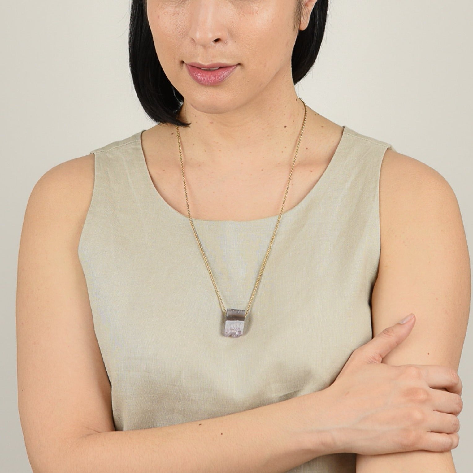 Model from waist up with mid tone skin and shoulder length black hair wearing necklace.