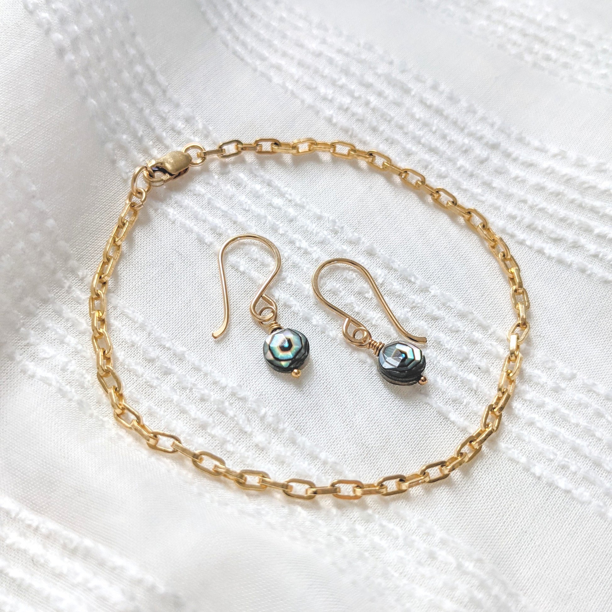 Flatlay image on textured summery white cotton paired with the Luxe Bracelet in 14K gold fill and Star Facet Earrings in Abalone with 14K gold fill details from Berlin jewelry designer Zurina Ketola