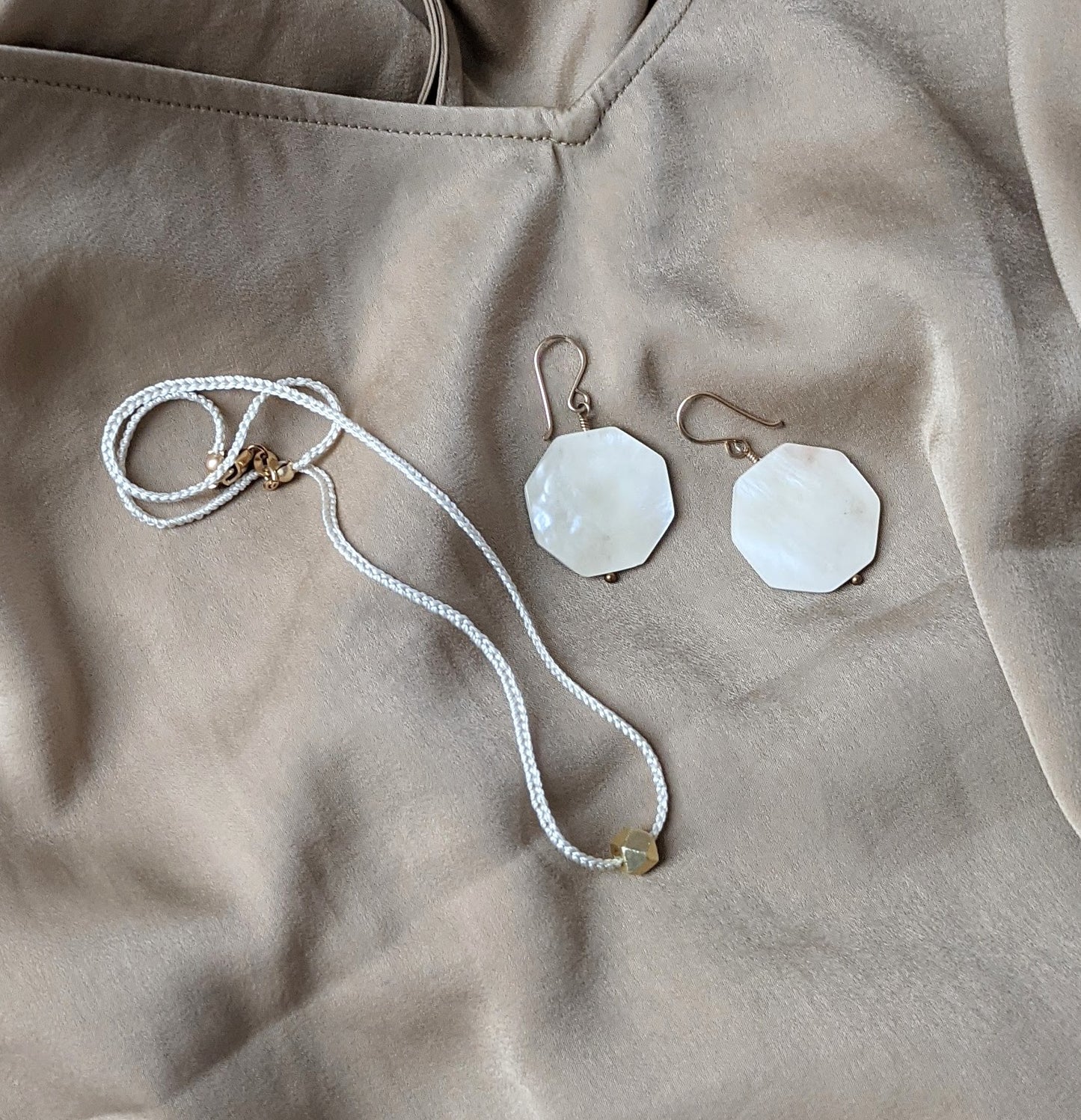 Flatlay image featuring a silky beige cami paired with the Silk Solitaire Necklace in ecru silk and gold details along with Kabebe Hexagon Earrings in 14K gold fill from Berlin jewelry designer Zurina Ketola.