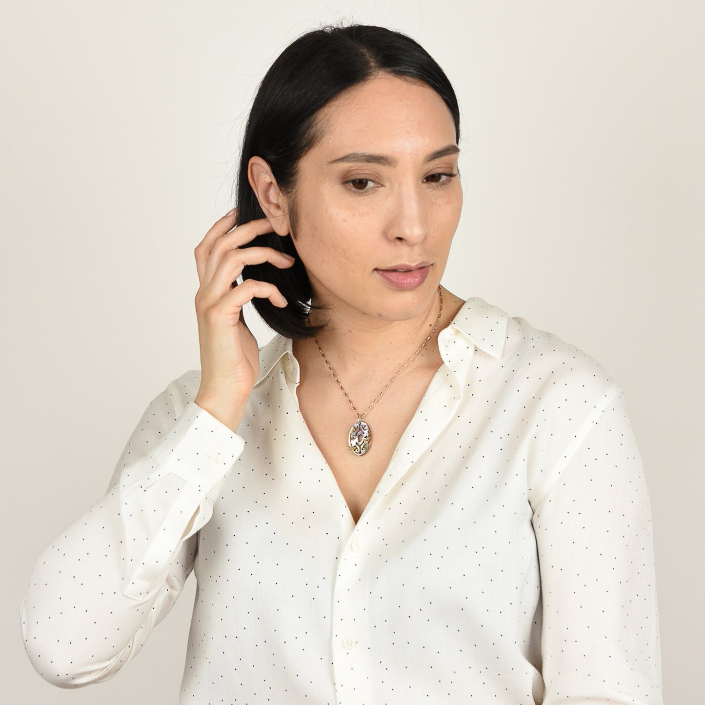 Model with mid tone skin and shoulder length black hair wearing carved abalone necklace on beaded gold fill  chain.