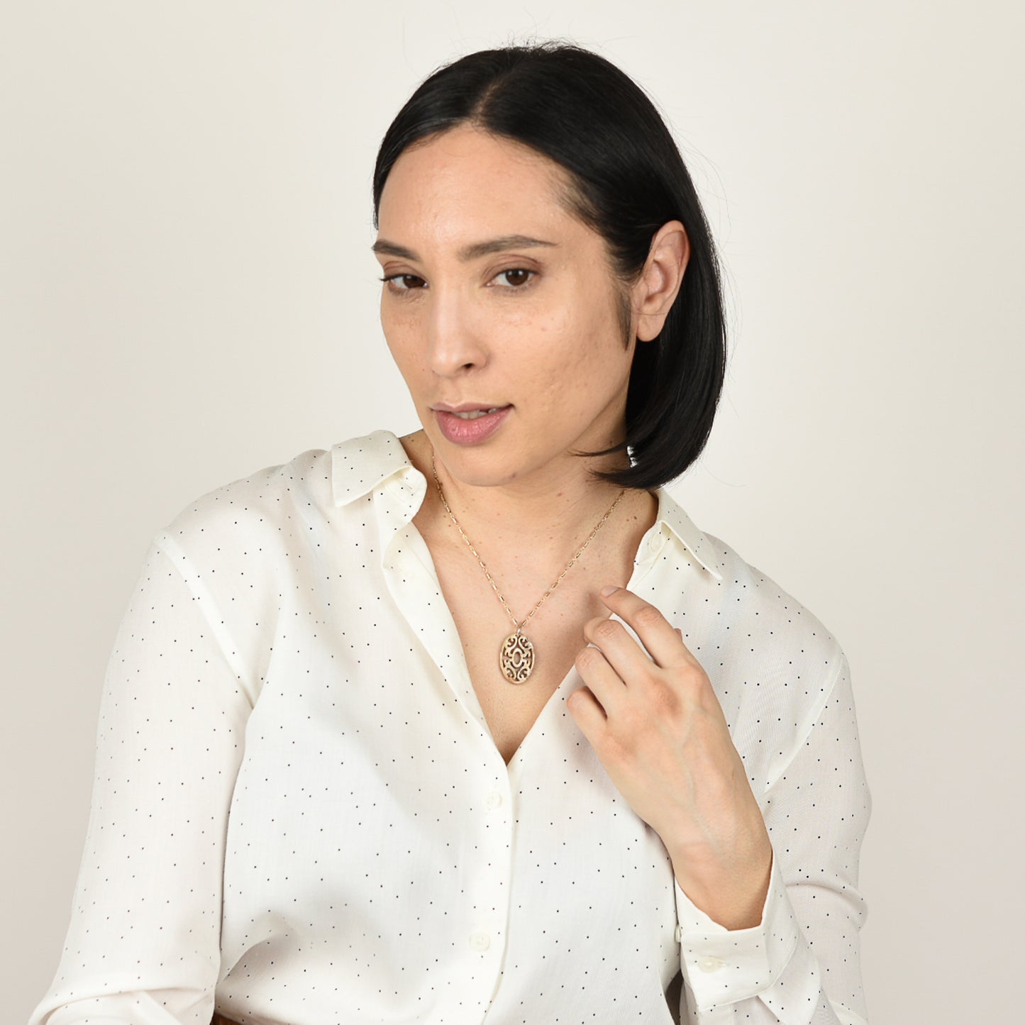 Model with mid tone skin and shoulder length black hair wearing carved abalone necklace on beaded gold fill  chain.