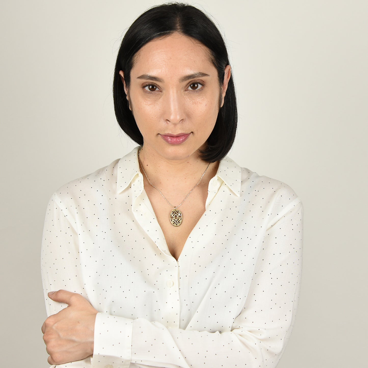 Model with mid tone skin and shoulder length black hair wearing carved abalone necklace on silver chain. 