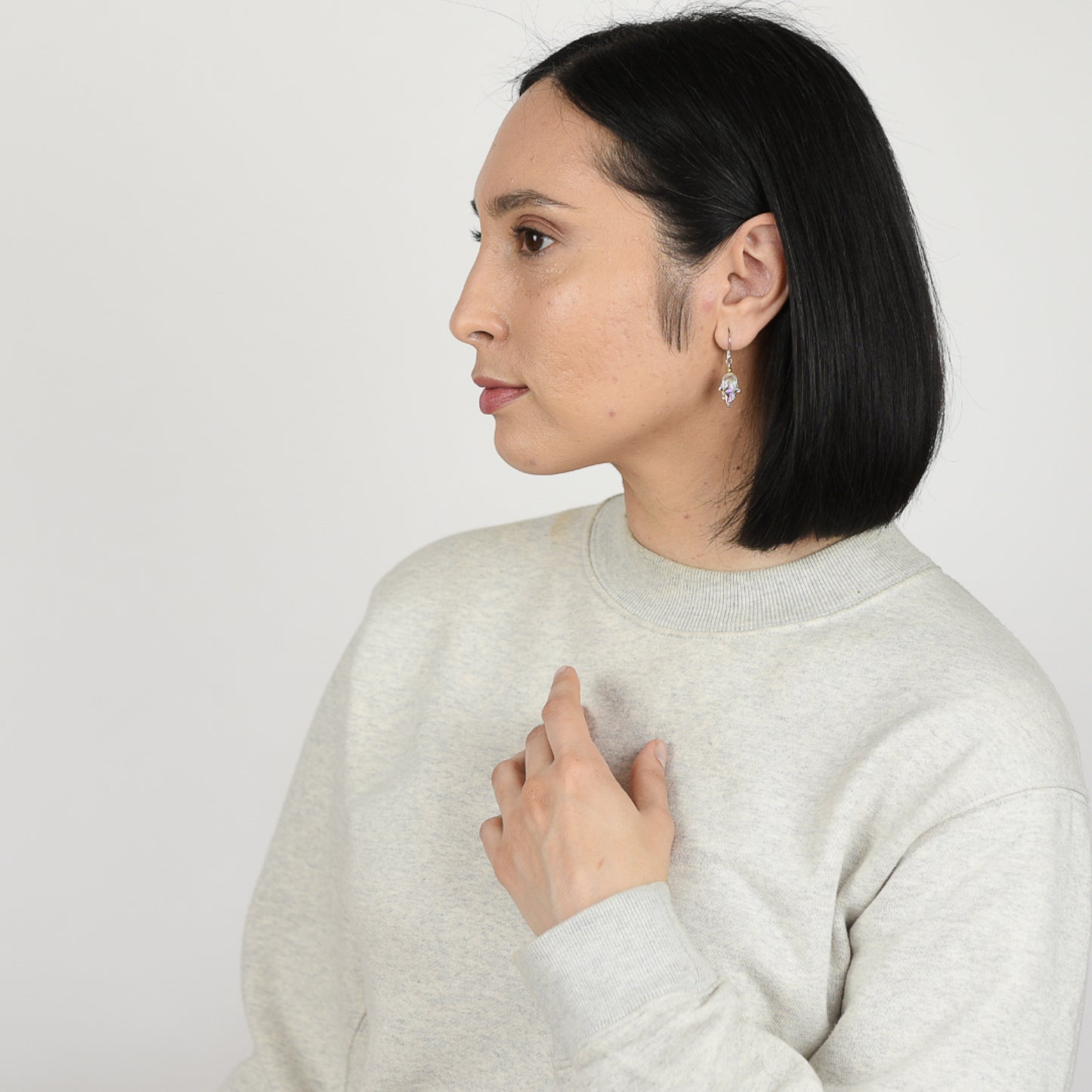 Model wearing abalone hamsa earrings in sterling silver with gold plated hematite detail. 