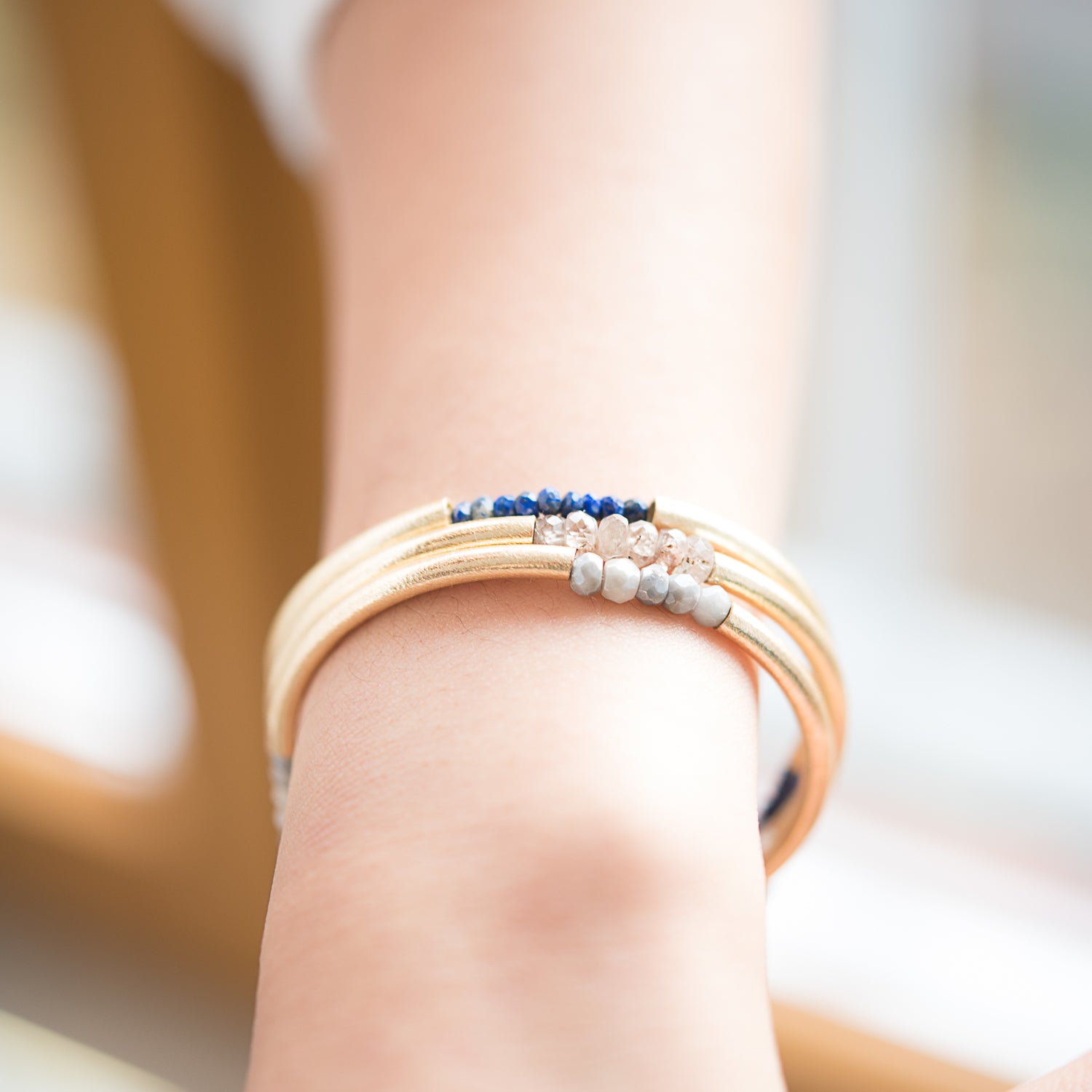 Close up of a models arm and wrist, wearing three triplet bangles. One in lapis, zircon, and gray moonstone.